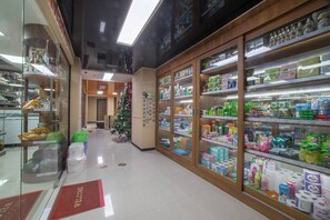 Un rayon de pharmacie avec des étagères remplies de divers produits, un sapin de Noël et un paillasson.