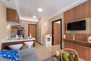 Una cocina moderna con lavadora incorporada, un comedor con mesa y sillas blancas, y una sala de estar con sofá y televisor montado en la pared.