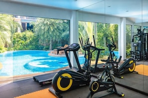 Un gimnasio con equipo de ejercicio y vistas a una piscina.