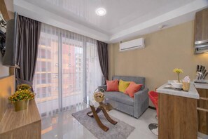 Una sala moderna con un sofá gris, una mesa de centro de vidrio y una zona de cocina con encimera gris.