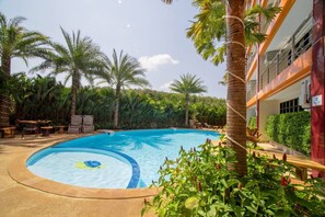 A swimming pool with a circular design, surrounded by palm trees and greenery, with a building adjacent to the pool.