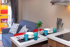 Een eetgedeelte met een tafel gedekt voor twee personen, een kleine plant en een keukenhoek met een vaatwasser.