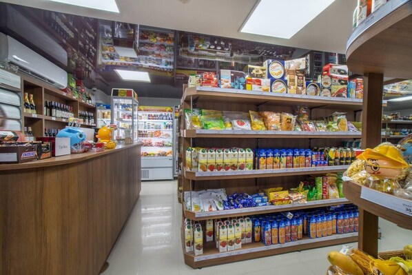 A grocery store interior with shelves stocked with various products, a refrigerated section, and a counter with snacks.