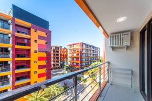 Een balkon met uitzicht op kleurrijke appartementenflats, een metalen hekwerk en een airconditioning op de muur.