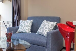 A grey sofa with patterned cushions, a glass table with a vase, and red chairs.