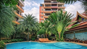 Una piscina circondata da palme e lettini, con un edificio a più piani sullo sfondo.