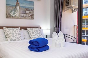 Habitación de hotel con cama, almohadas, un cuadro y ventana con vista a un edificio.