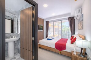 A modern hotel room with a marble bathroom, a bed with a red blanket, and a TV on the wall.