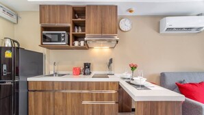 Uma cozinha compacta com armários de madeira, micro-ondas, máquina de café e um relógio na parede.