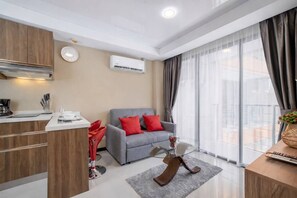 A modern living room with a grey sofa, red cushions, a wooden coffee table, and a large window with curtains.