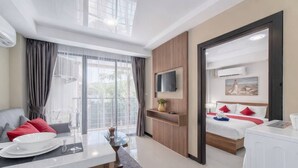 Quarto de hotel com cama, televisão na parede, área de jantar com mesa e cadeiras, e vista pela janela.