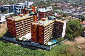 A multi-story building with balconies, a rooftop pool, and a sign indicating a rent sale.