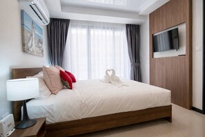 A hotel room with a bed, a flat-screen TV, a painting, and a window with curtains.