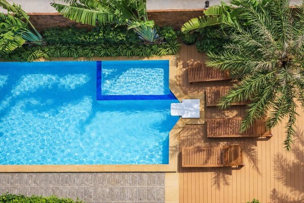 An aerial view of a swimming pool with a wooden deck, lounge chairs, and tropical plants.