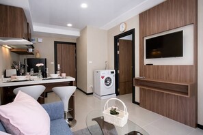 A modern kitchen with a dining area, a washing machine, and a flat-screen TV mounted on the wall.