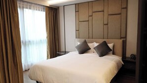 Una camera d'albergo con un letto grande, una testiera con motivo geometrico e un comodino con una sveglia.