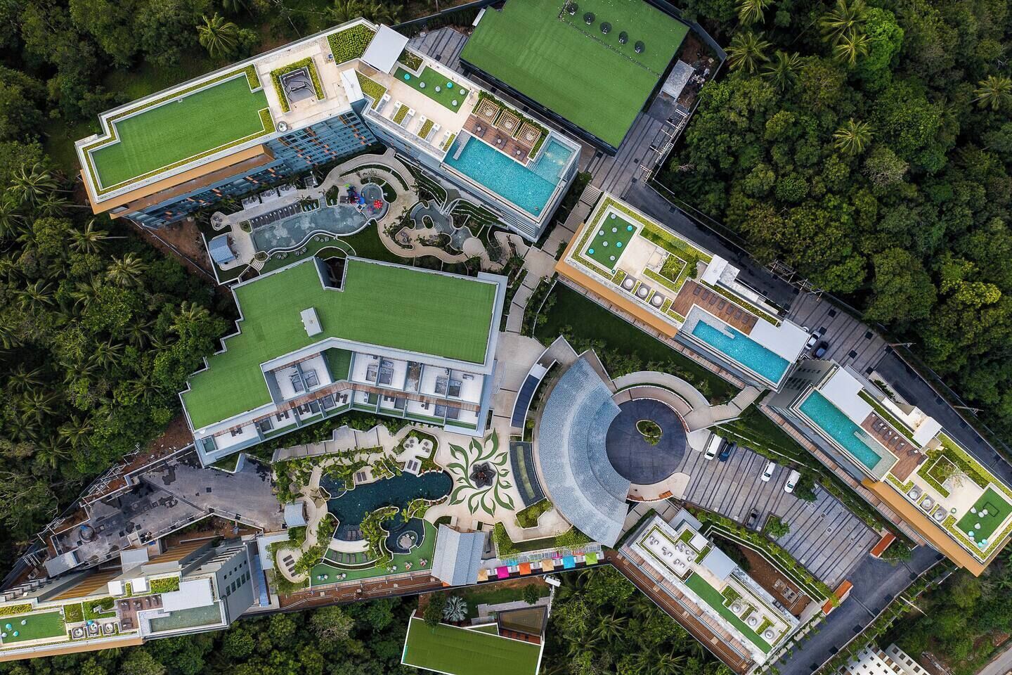 Eine Vogelperspektive auf ein Hotel mit mehreren Schwimmbecken, grünen Rasenflächen und einem zentralen, kreisförmigen Innenhof.