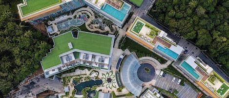 Vista aérea de un hotel con múltiples piscinas, césped verde y un patio circular central.