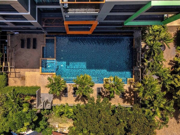 A rooftop pool with a blue mosaic floor, surrounded by palm trees and greenery.