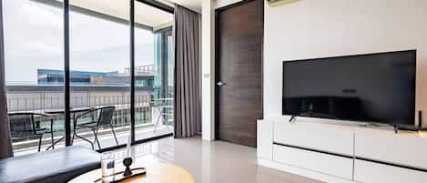 A modern hotel room with a balcony, a flat-screen TV, and a dining area.