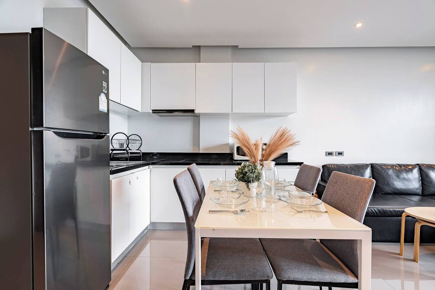 Una cocina moderna con comedor, que presenta un refrigerador de acero inoxidable, gabinetes blancos, una encimera negra y una mesa de comedor para cuatro.