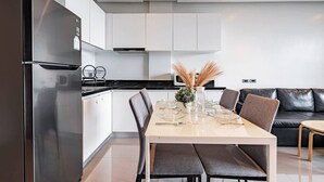 Een moderne keuken met een eethoek, voorzien van een roestvrijstalen koelkast, witte kasten, een zwart aanrechtblad en een eettafel gedekt voor vier personen.