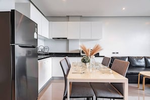 Una cocina moderna con comedor, que presenta un refrigerador de acero inoxidable, gabinetes blancos, una encimera negra y una mesa de comedor para cuatro.