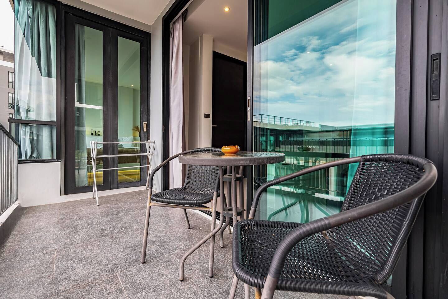 Un balcón con una mesa y sillas, una puerta de vidrio que da a una habitación y vistas a un edificio.