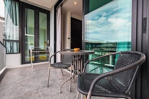 A balcony with a table and chairs, a glass door leading to a room, and a view of a building.