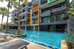 A modern hotel with a swimming pool, multiple balconies, and outdoor seating areas.