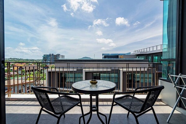 A balcony with a round table and two chairs, overlooking a cityscape with modern buildings and a clear sky. - Suite Lumi 2bedroom Rooftop pool Relife Nai Harn (Rawai)