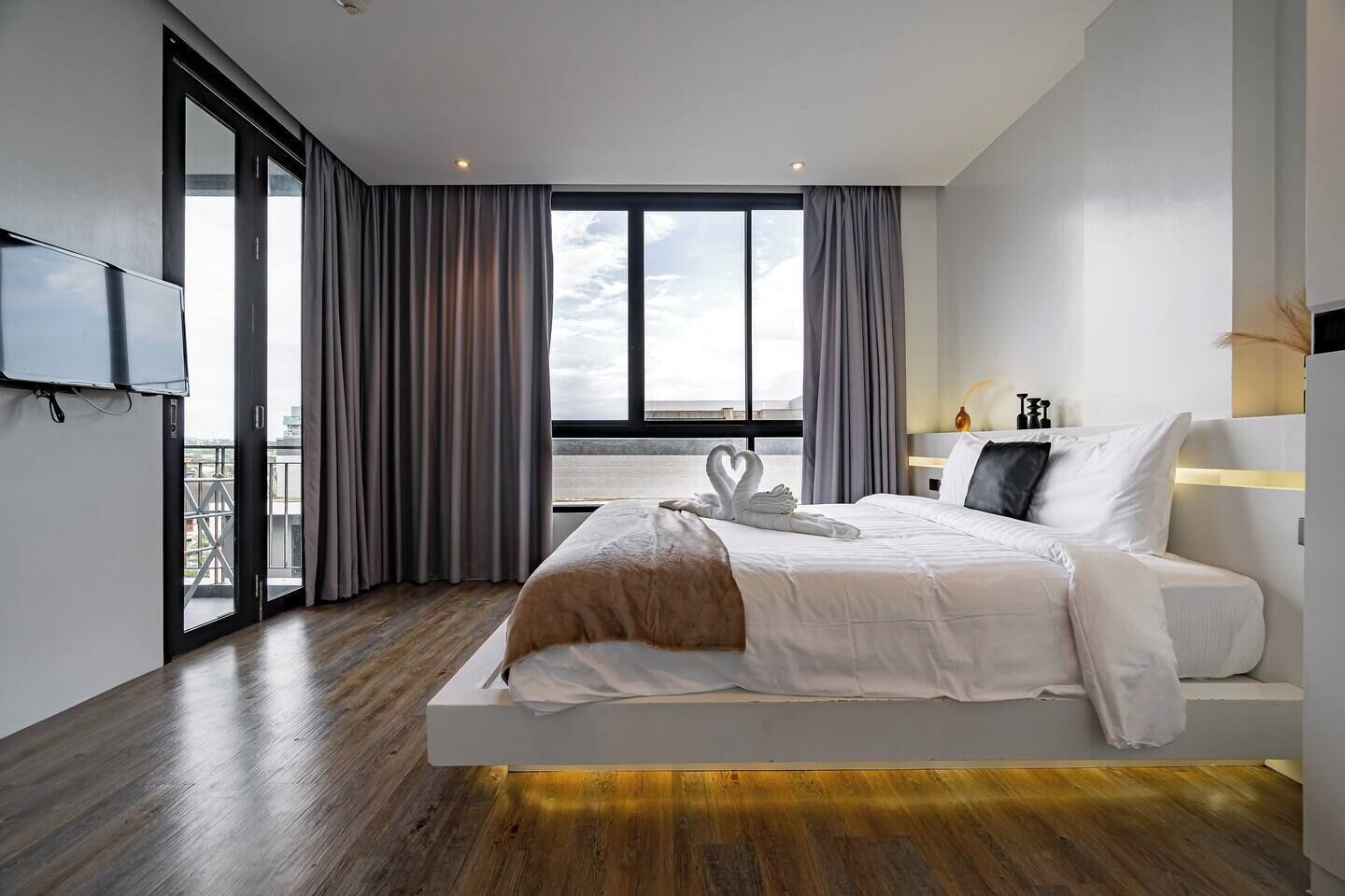 A modern hotel room with a large bed, a flat-screen TV, a view of the city, and a balcony.