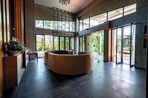 Un espace d’accueil moderne, doté d’un comptoir de réception central en bois, de grandes fenêtres et d’une vue sur la verdure environnante.