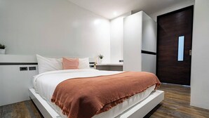 Een moderne slaapkamer met een groot bed, een houten vloer, een donkere deur en een witte garderobe.