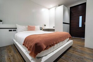 Un dormitorio moderno con una cama grande, suelo de madera, una puerta oscura y un armario blanco.