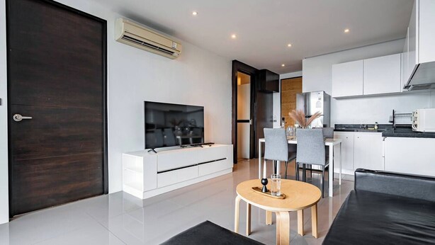 Een moderne woonkamer met een flatscreen televisie, een eethoek met een ronde tafel, en een keuken met witte kasten.