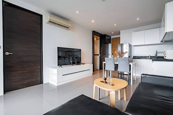 Una sala de estar moderna con un televisor de pantalla plana, un comedor con una mesa redonda y una cocina con gabinetes blancos.