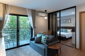 Une chambre d’hôtel moderne dotée d’un balcon, d’un canapé, d’une petite table, d’un lit et d’une porte-fenêtre coulissante.