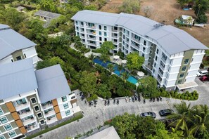 A multi-story hotel with a swimming pool surrounded by lush greenery. - Suite Lumaire 1br | Pool view | the title v rawai (Rawai)