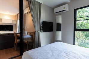 A hotel room with a bed, a desk with a chair, a TV, and a window with a view of trees.