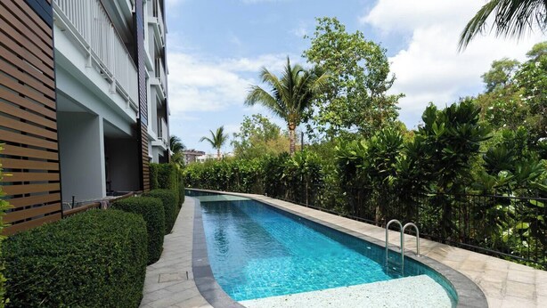 A swimming pool with a curved edge, surrounded by a paved walkway and lush greenery.