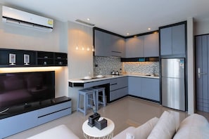 A modern kitchen with a built-in oven, a refrigerator, and a dining area with bar stools. - Suite Sol 1br | sunset rooftop | Citygate Kamala (Tambon Kammala)