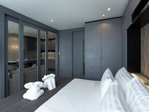 Une chambre d’hôtel moderne dotée d’un grand lit, d’un coin salon avec un canapé et des fauteuils, d’une armoire et d’une salle de bain visible à travers une paroi en verre.