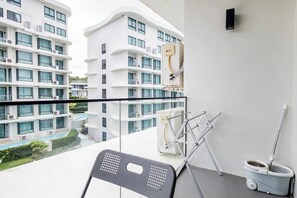 Un balcón con vistas a una piscina y edificios cercanos, una silla, un trapeador y un altavoz montado en la pared.