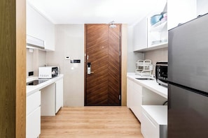 A modern kitchen with white cabinetry, a wooden door, and stainless steel appliances.