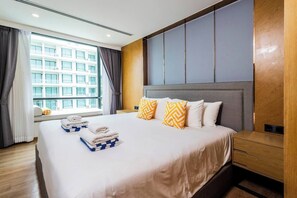 Habitación de hotel con una cama grande, una mesita de noche de madera, una ventana con cortinas y vistas a un edificio.