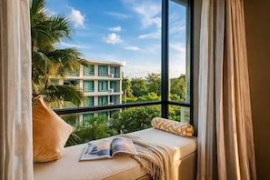 A balcony with a view of a building and greenery, a sofa with cushions, and a book.