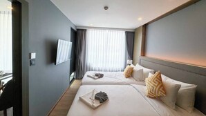 A hotel room with two beds, a flat-screen TV, a desk, and a window with curtains. - Suite Solis 2br | Resort pool view | 300m to rawai (Rawai)