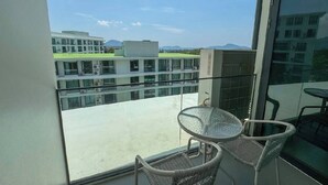 A balcony with a glass table and chairs, overlooking a building and distant landscape. - Suite Solis 2br | Resort pool view | 300m to rawai (Rawai)