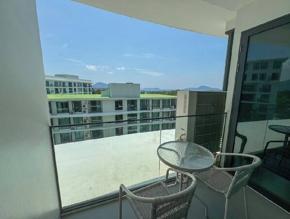 Un balcón con mesa y sillas de vidrio, con vistas a un edificio y un paisaje distante.